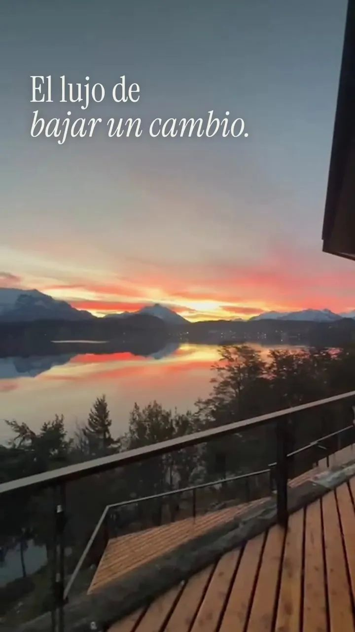 Desde un balcón de madera, los ventanales reflejan las montañas y el atardecer sobre el agua. En pantalla: El lujo de bajar un cambio.