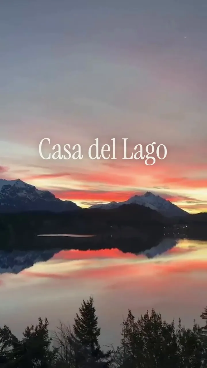 Las montañas y el bosque se reflejan en el lago al atardecer. El título aparece sobre la cordillera: Casa del Lago. Península San Pedro · Bariloche.