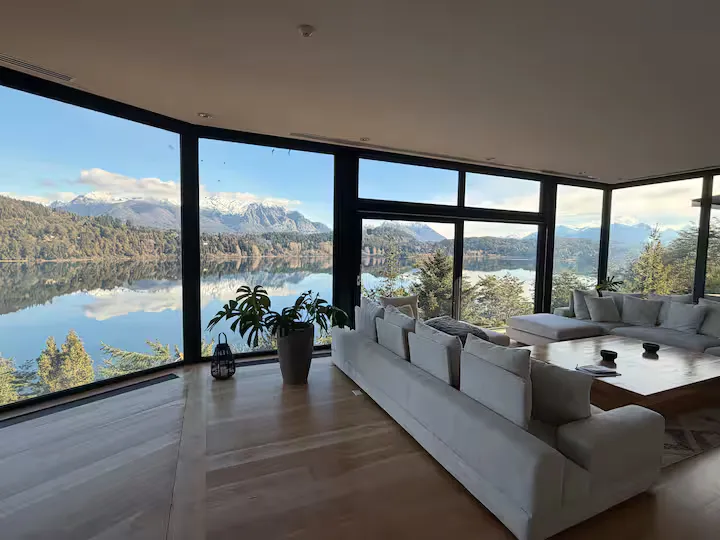 Living con sillones blancos y ventanales de piso a techo sobre el lago