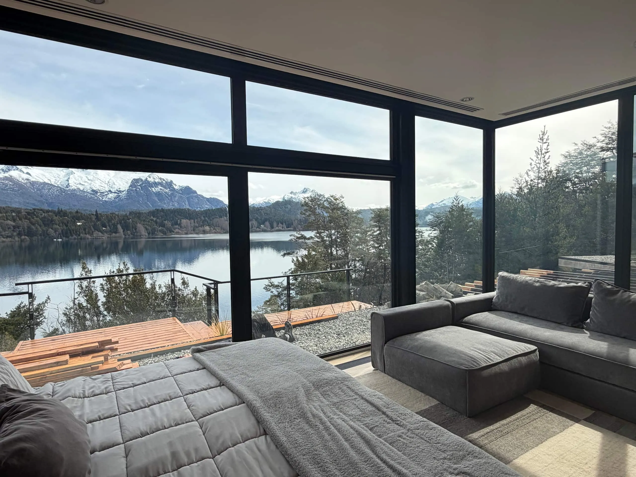 Dormitorio con ventanales en esquina, sillón gris y vista al lago y la cordillera nevada